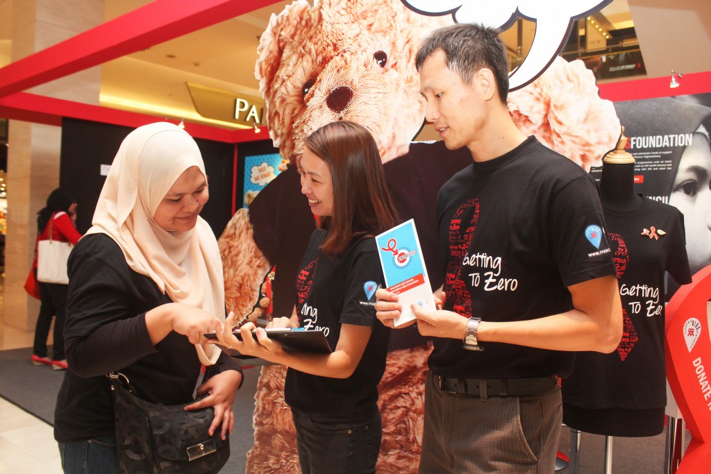 A visitor (left) participates in a HIV knowledge survey conducted by Standard Chartered Scope International volunteers at the Red Ribbon Popup Store in Pavilion Kuala Lumpur. Photo © 2016 Malaysian AIDS Council & Malaysian AIDS Foundation. 